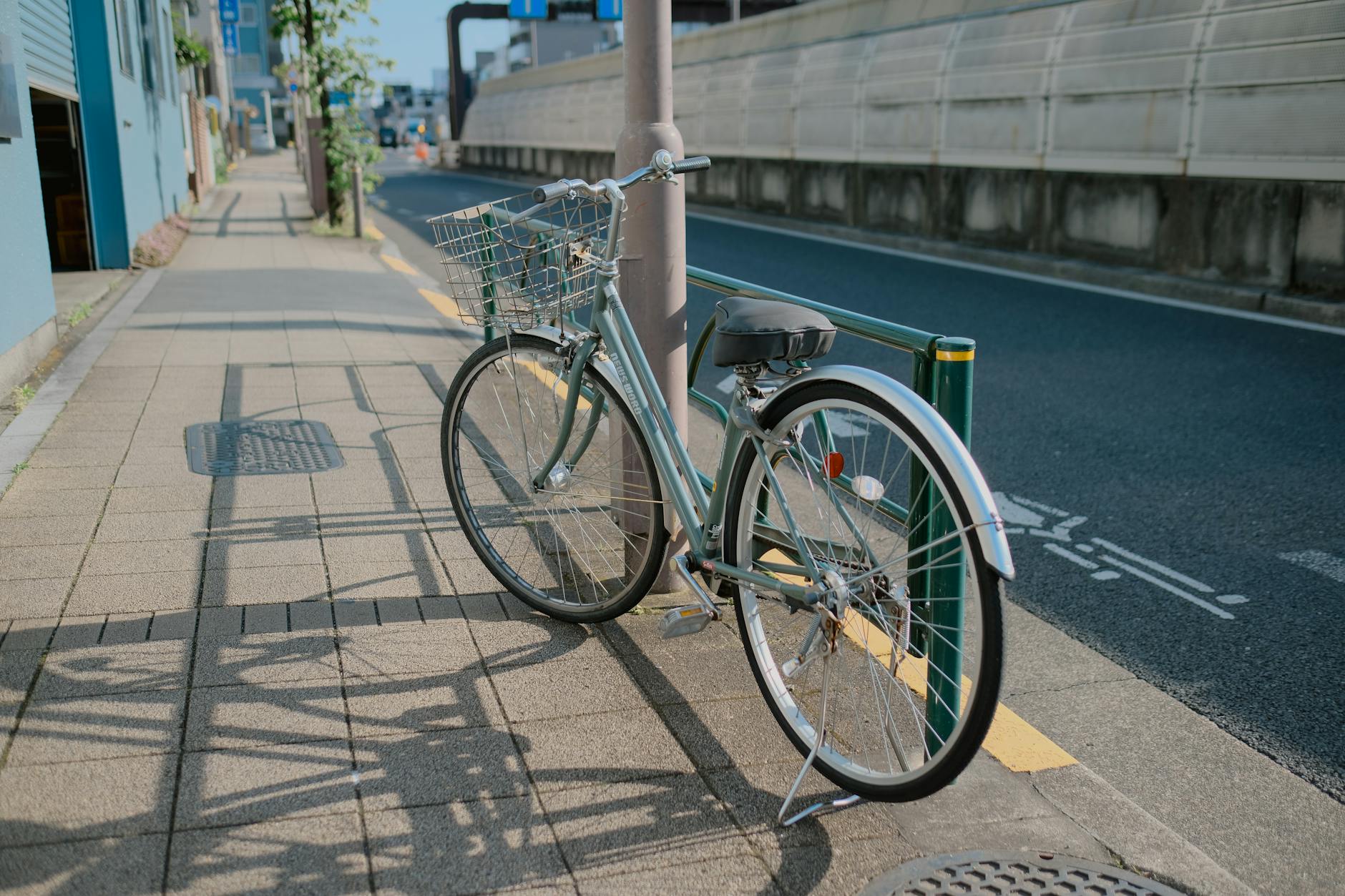 A bicycle with a basket parked on a sunlit sidewalk in Tokyo, Japan.