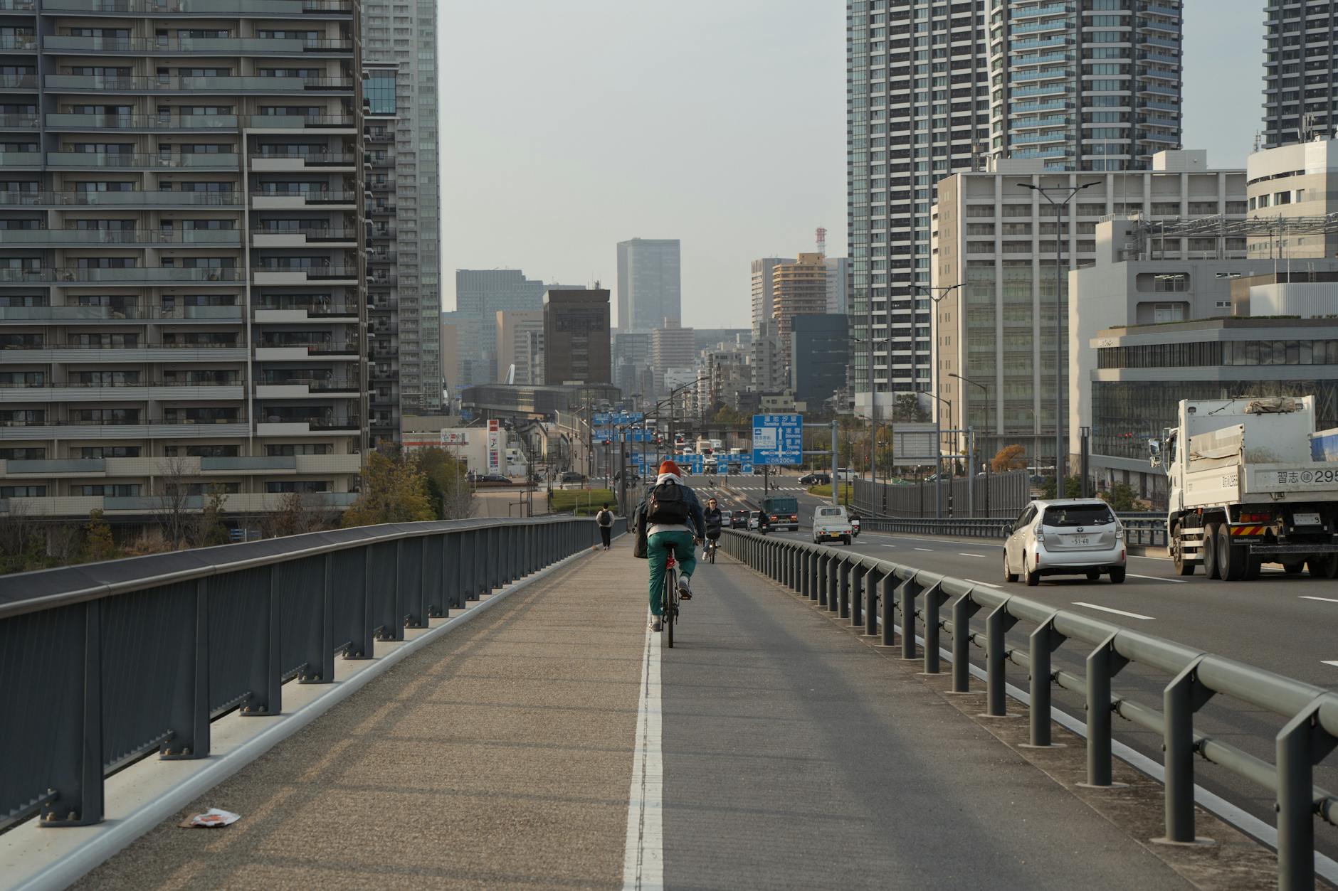 Cyclist riding on a Tokyo highway, surrounded by tall buildings under a clear sky.