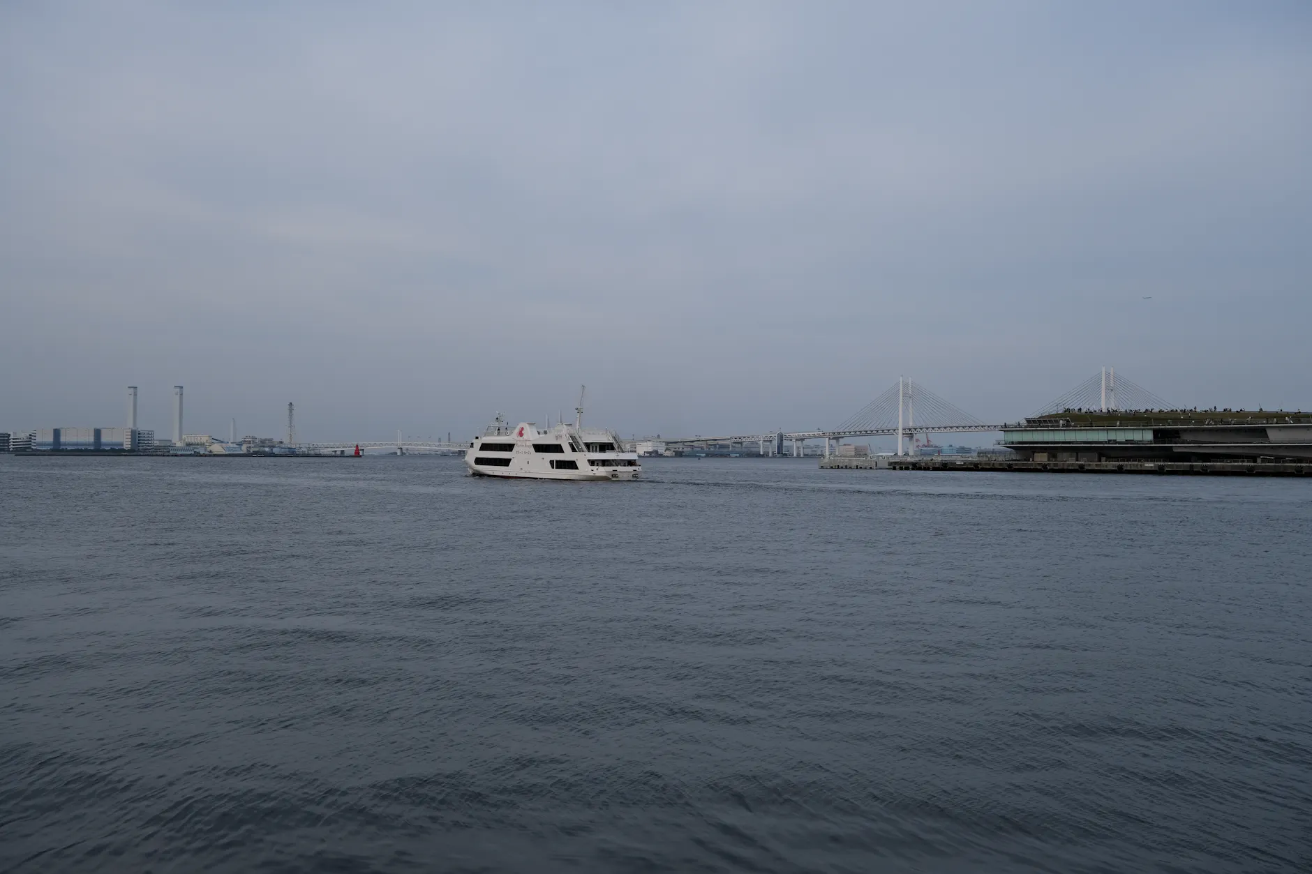 A serene view of a cruise ship in Yokohama Bay with the iconic bridge in the background.